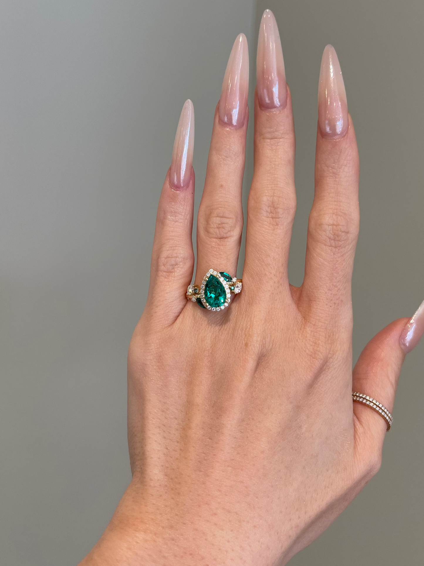 Hand wearing a ring with a green gemstone against a neutral background