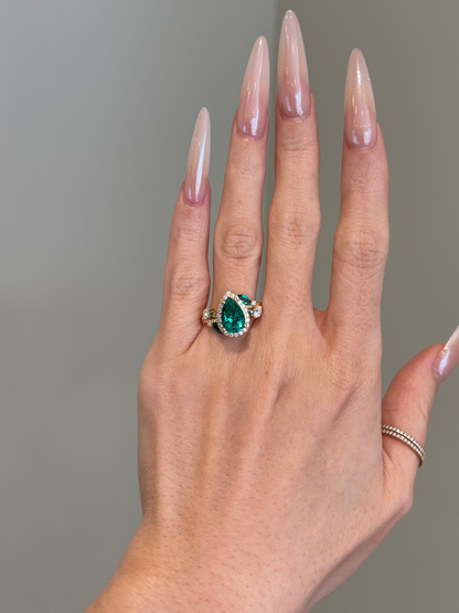 Hand wearing a ring with a green gemstone against a neutral background