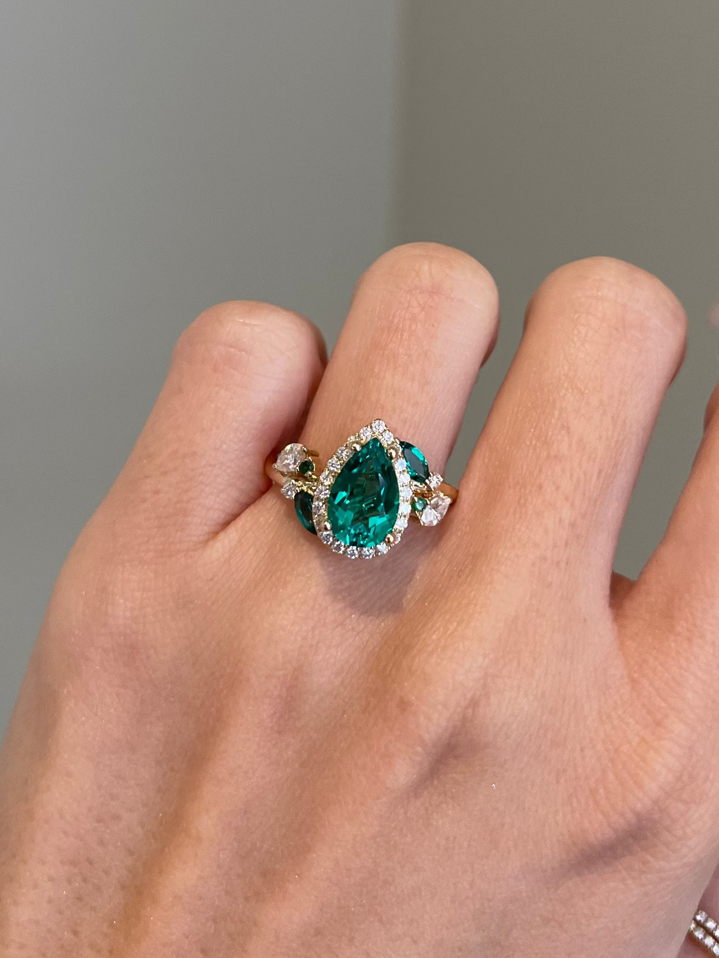 Hand wearing a ring with a green gemstone on a neutral background
