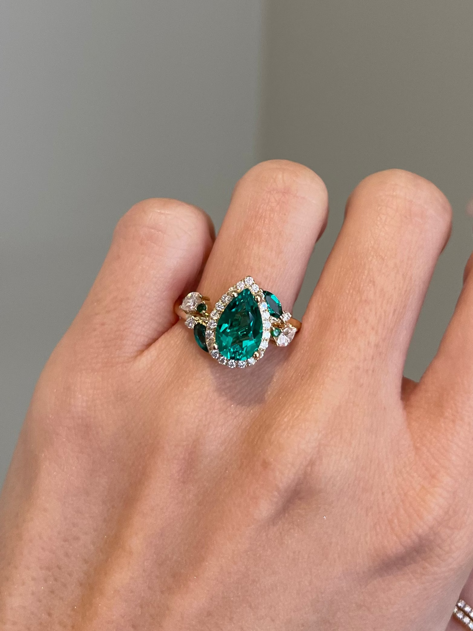 Hand wearing a ring with a green gemstone on a neutral background