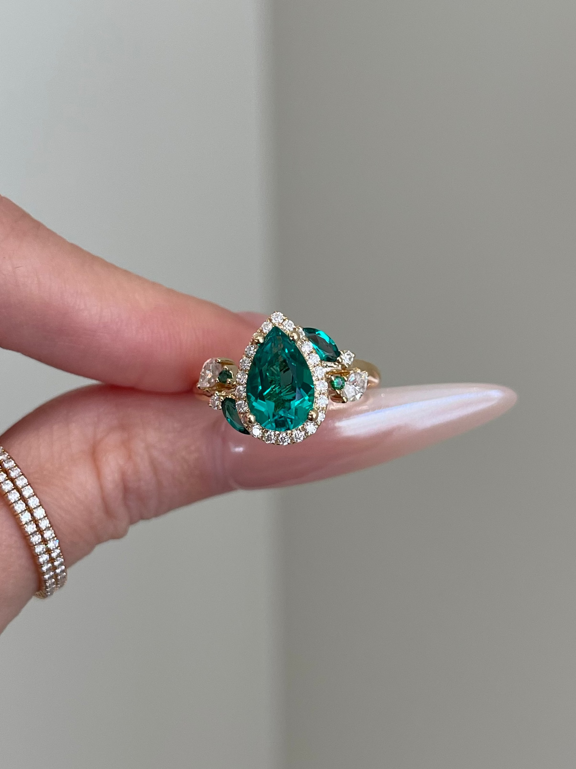 Teardrop emerald ring on a hand with a neutral background
